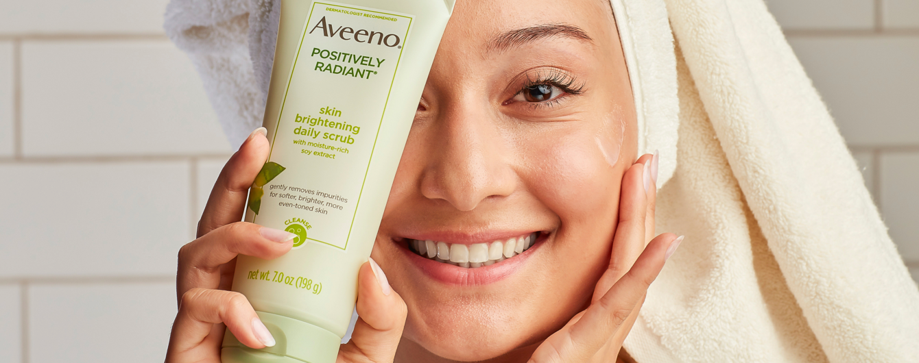 Woman applying Aveeno skin brightening daily scrub to face