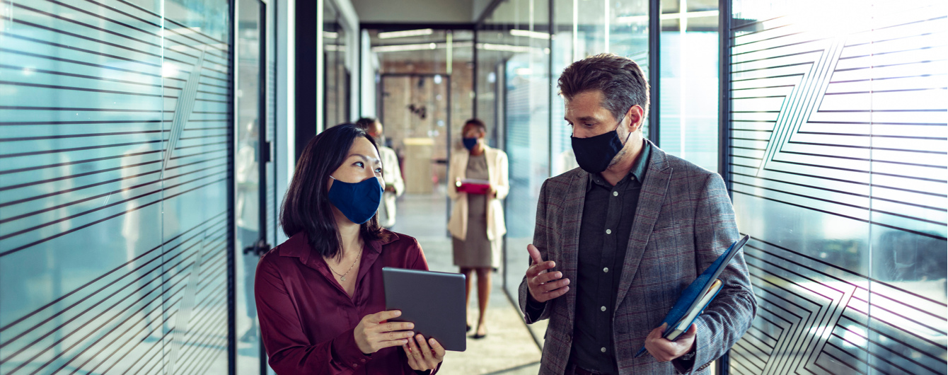 Man and woman having discussion in hallway wearing masks